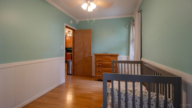 bedroom featuring crown molding, ceiling fan, a crib, and light wood-type flooring