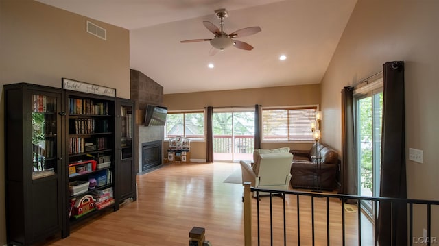 living room featuring a tile fireplace, ceiling fan, light hardwood / wood-style flooring, and high vaulted ceiling