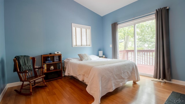 bedroom with access to exterior, wood-type flooring, and vaulted ceiling