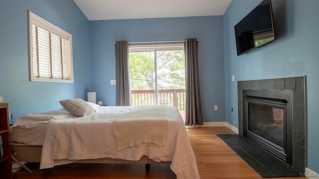 bedroom with hardwood / wood-style floors, a tile fireplace, and multiple windows