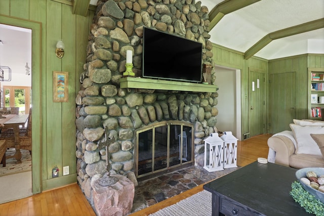 living room with hardwood / wood-style floors, vaulted ceiling with beams, wood walls, and a stone fireplace