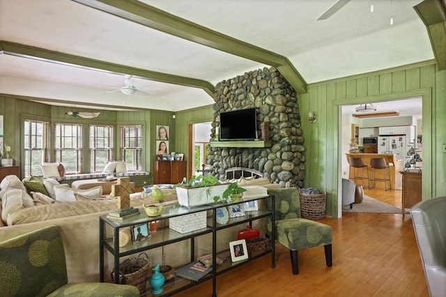 living room with ceiling fan, vaulted ceiling with beams, wooden walls, a fireplace, and hardwood / wood-style flooring