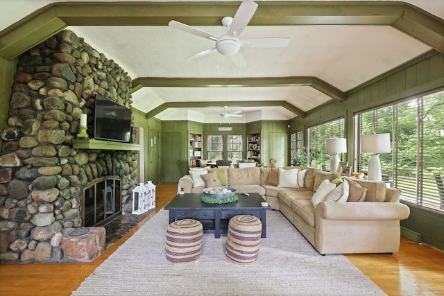 living room with vaulted ceiling with beams, light hardwood / wood-style floors, a stone fireplace, and plenty of natural light