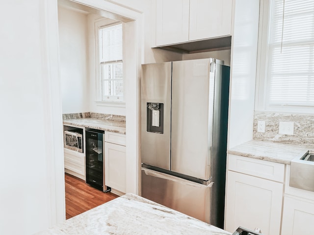 488 Parkview Dr, Detroit, MI 48214 - kitchen featuring appliances with stainless steel finishes, wine cooler, white cabinetry, wood finished floors, and light stone counters