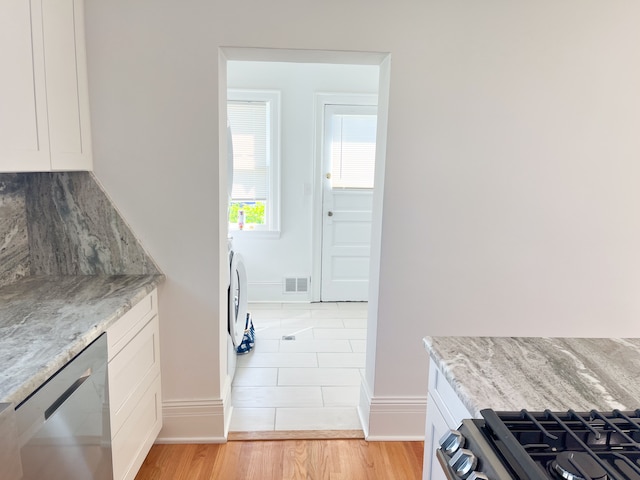 kitchen with white cabinets, stainless steel stove, light hardwood / wood-style flooring, and light stone countertops