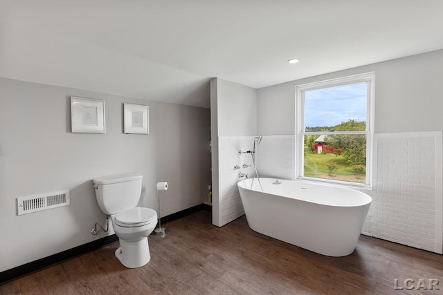 bathroom featuring toilet, wood-type flooring, a tub, and tile walls