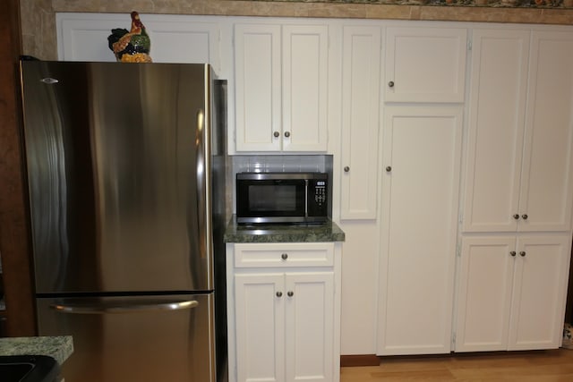 kitchen with dark stone counters, light hardwood / wood-style flooring, white cabinets, and stainless steel appliances