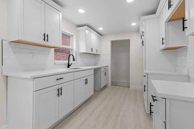 kitchen with decorative backsplash, light wood-type flooring, white cabinetry, and sink