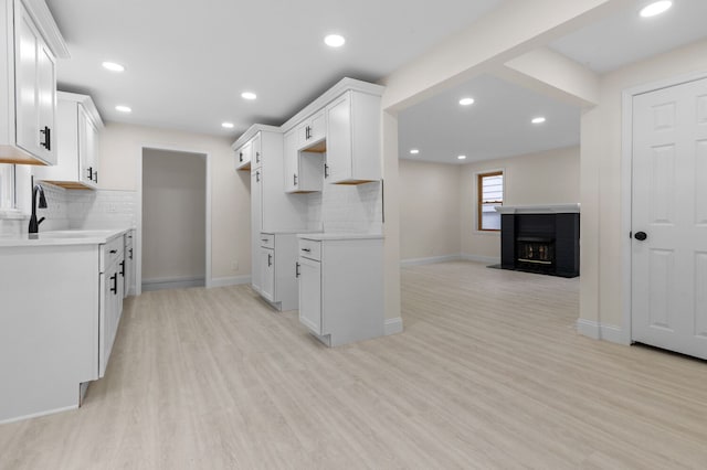 kitchen with decorative backsplash, a brick fireplace, light hardwood / wood-style floors, and white cabinetry