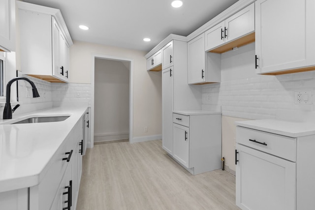 kitchen with backsplash, sink, white cabinets, and light hardwood / wood-style flooring