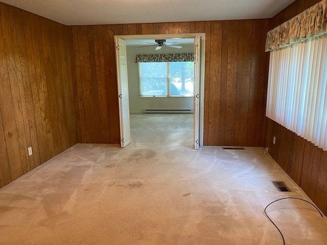 carpeted spare room with ceiling fan, wood walls, and a baseboard radiator