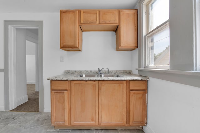 kitchen with light stone countertops, light brown cabinets, light colored carpet, and sink