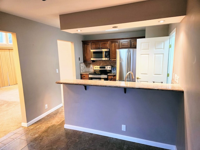 kitchen with kitchen peninsula, tasteful backsplash, a breakfast bar, stainless steel appliances, and sink