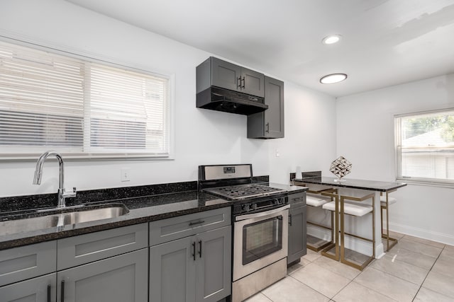 kitchen featuring sink, stainless steel gas range, dark stone counters, gray cabinets, and light tile patterned floors