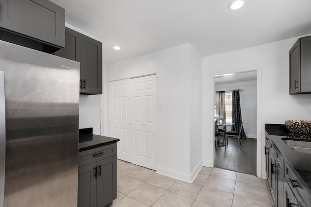 kitchen featuring gray cabinets, stainless steel fridge, light tile patterned flooring, and dark stone counters