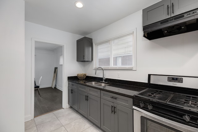 kitchen with gray cabinetry, stainless steel gas stove, sink, dark stone counters, and light tile patterned floors