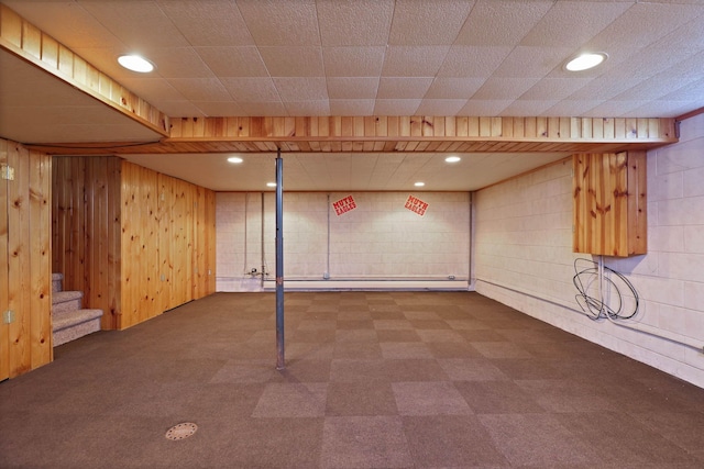 finished below grade area with stairway, wooden walls, recessed lighting, and tile patterned floors