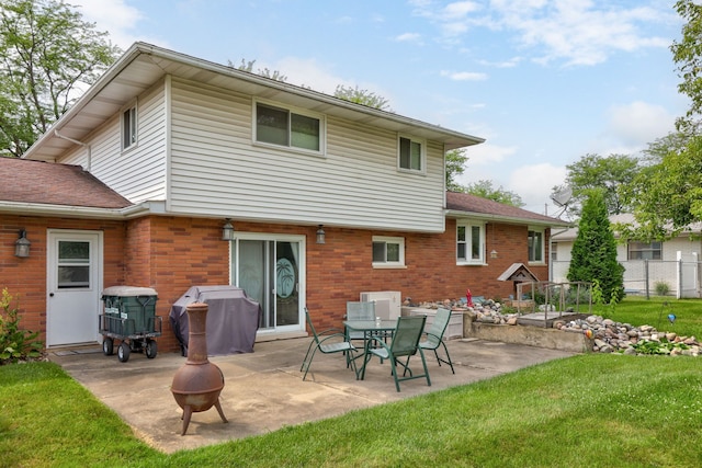 back of property with brick siding, fence, an outdoor fire pit, a lawn, and a patio area