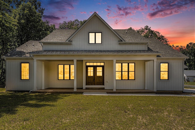 back house at dusk featuring covered porch and a lawn