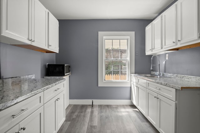 kitchen featuring hardwood / wood-style flooring, light stone countertops, white cabinetry, and sink