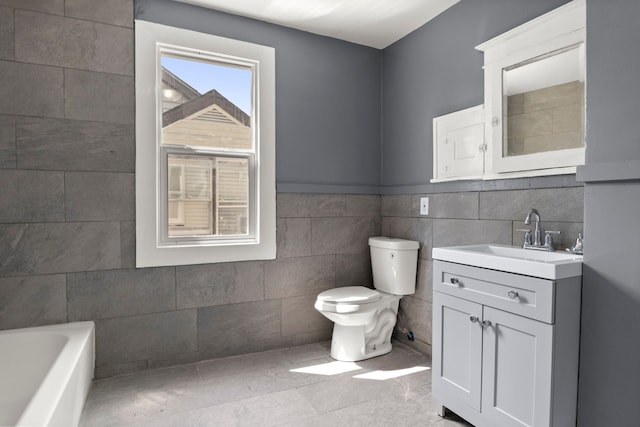 bathroom featuring tile patterned floors, vanity, a bath, tile walls, and toilet