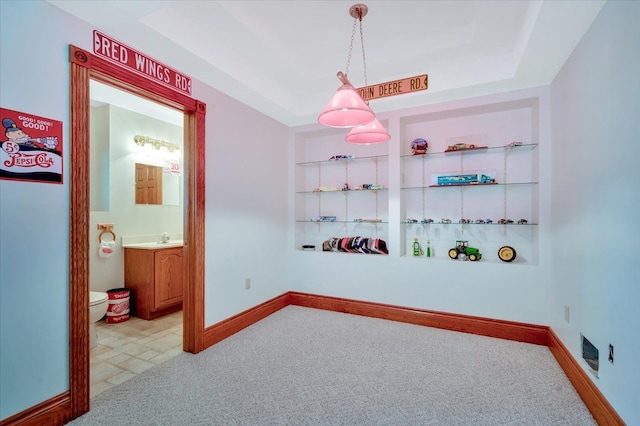 bedroom with light colored carpet, ensuite bath, a tray ceiling, and sink