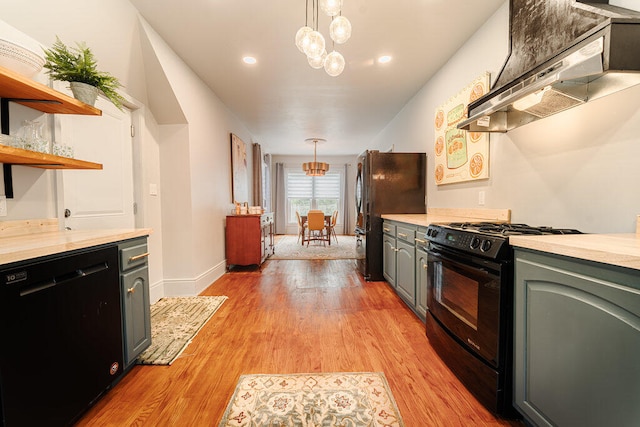 kitchen with black appliances, wall chimney exhaust hood, light hardwood / wood-style floors, and hanging light fixtures