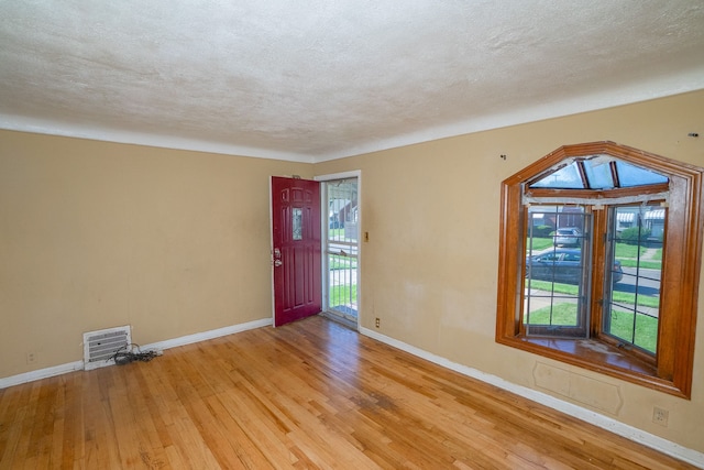 empty room with a textured ceiling and light hardwood / wood-style flooring