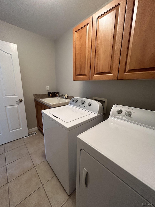 clothes washing area with light tile patterned floors, washing machine and dryer, cabinets, and sink