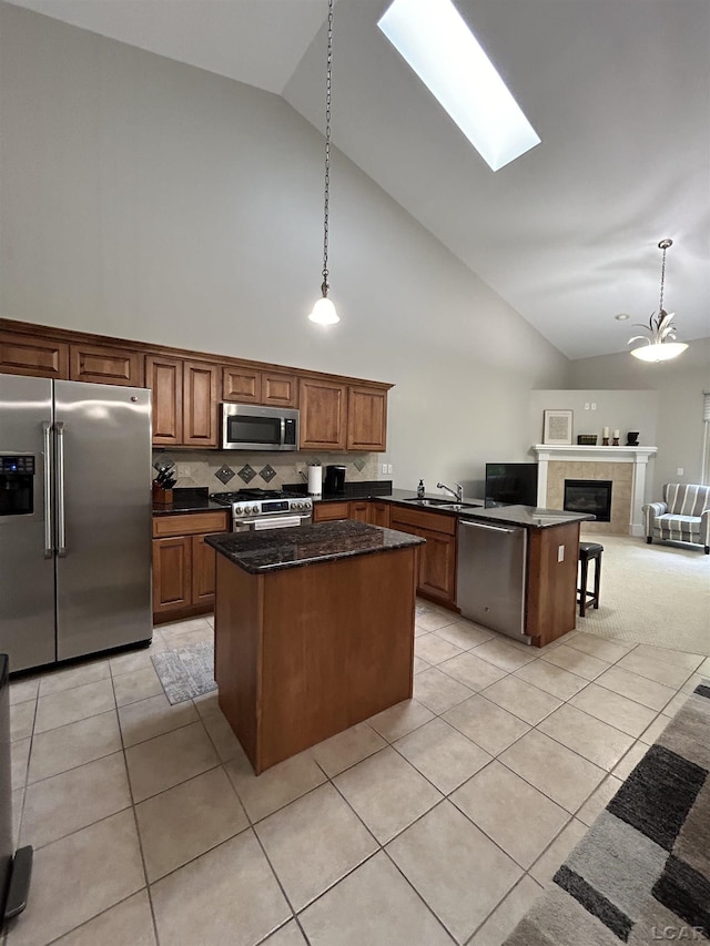 kitchen featuring decorative light fixtures, a tiled fireplace, tasteful backsplash, a kitchen island, and appliances with stainless steel finishes