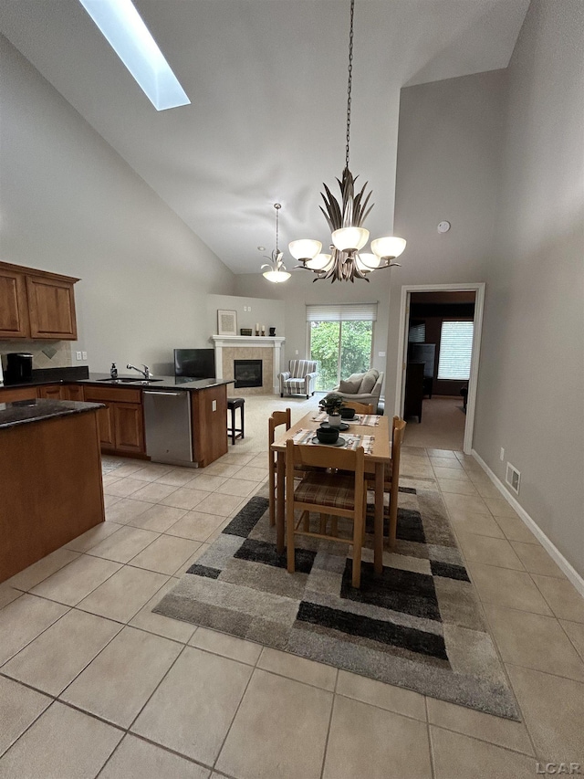 tiled dining room featuring a tile fireplace, a notable chandelier, high vaulted ceiling, a skylight, and sink