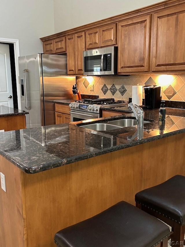 kitchen featuring appliances with stainless steel finishes, kitchen peninsula, dark stone counters, a breakfast bar, and decorative backsplash