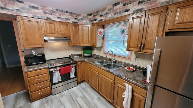 kitchen featuring appliances with stainless steel finishes, dark stone counters, brick wall, sink, and light hardwood / wood-style floors