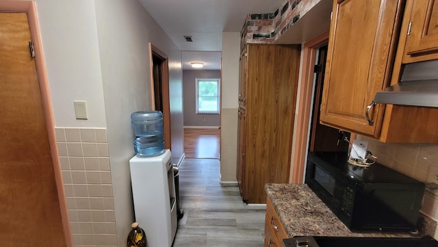 kitchen featuring extractor fan, light hardwood / wood-style floors, light stone counters, and tile walls