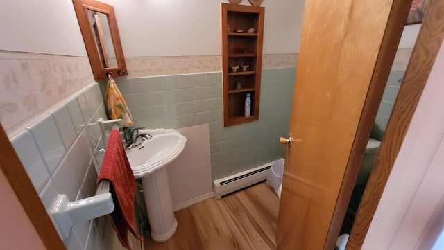 bathroom featuring sink, hardwood / wood-style flooring, baseboard heating, and tile walls