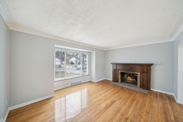 unfurnished living room featuring hardwood / wood-style flooring, crown molding, a textured ceiling, and a brick fireplace