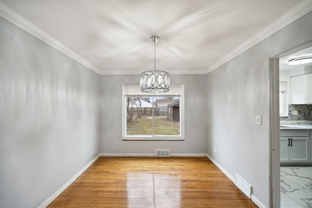 unfurnished dining area featuring a chandelier, crown molding, and light hardwood / wood-style floors