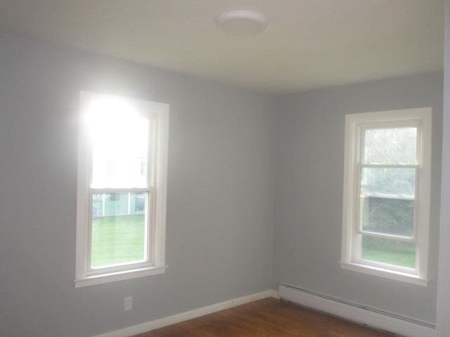 unfurnished room with plenty of natural light, dark hardwood / wood-style floors, and a baseboard radiator