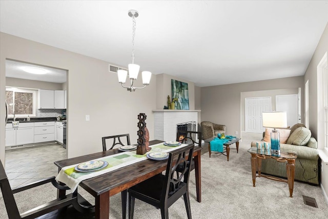 dining area with an inviting chandelier, light carpet, and a brick fireplace