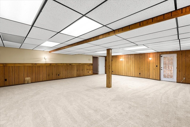 basement with carpet, a drop ceiling, and wood walls