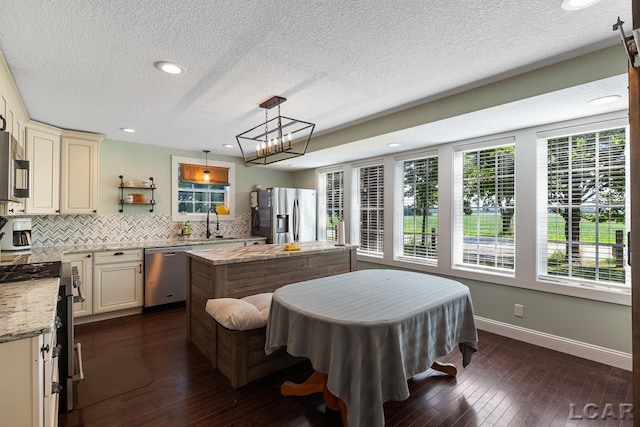 kitchen featuring light stone countertops, dark hardwood / wood-style flooring, decorative light fixtures, cream cabinetry, and appliances with stainless steel finishes