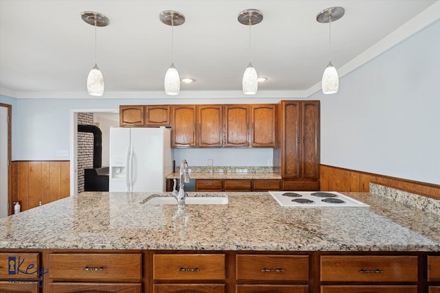 kitchen with wood walls, white appliances, sink, hanging light fixtures, and light stone counters