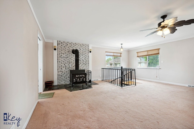 unfurnished living room featuring a wood stove, crown molding, carpet floors, and ceiling fan