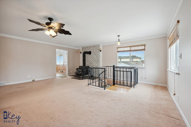 carpeted empty room with a wood stove, ceiling fan, and crown molding