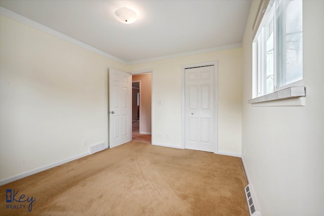 unfurnished bedroom featuring crown molding, light carpet, and a closet