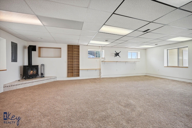 basement featuring carpet, a paneled ceiling, a wood stove, and electric panel