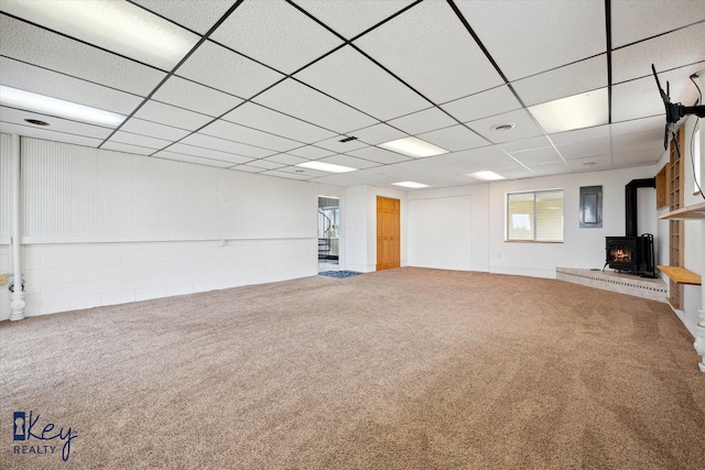 unfurnished living room featuring a wood stove, a paneled ceiling, electric panel, and carpet