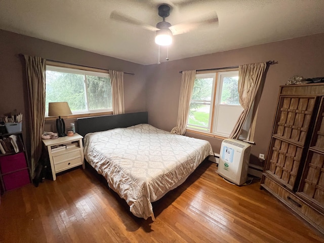 bedroom featuring wood-type flooring, ceiling fan, and a baseboard heating unit