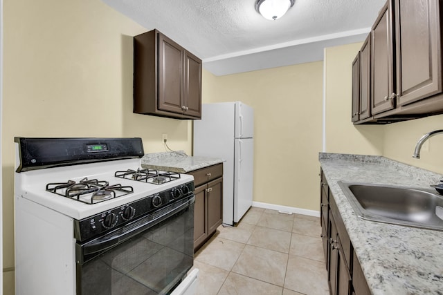 kitchen featuring dark brown cabinets, white appliances, a textured ceiling, sink, and light tile patterned floors