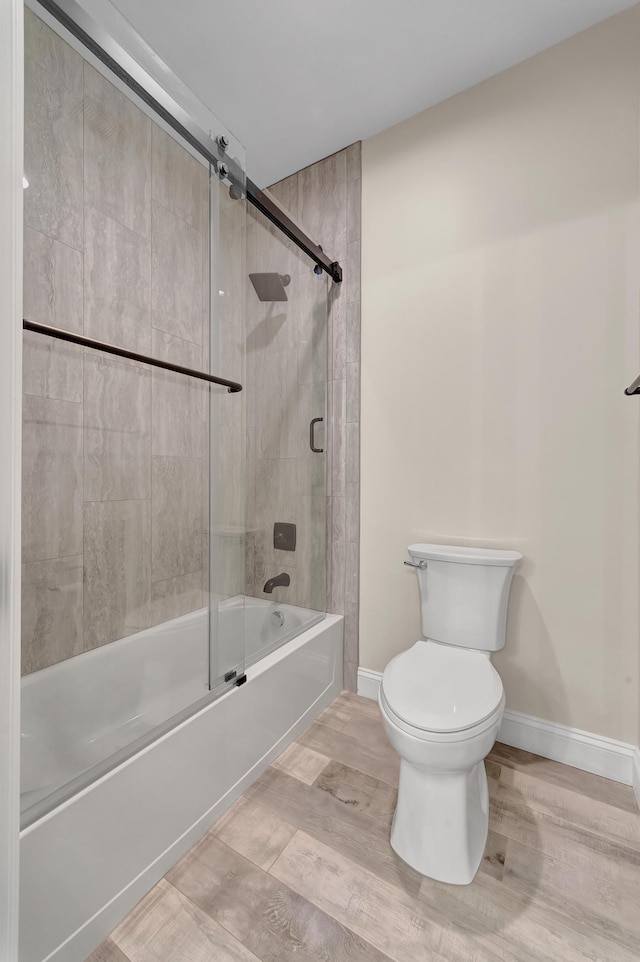 bathroom with combined bath / shower with glass door, hardwood / wood-style flooring, and toilet